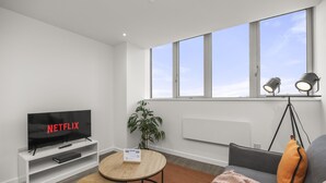 Ein modernes Wohnzimmer mit Flachbildfernseher, einem kleinen Tisch, einer Couch und einem großen Fenster mit Blick.