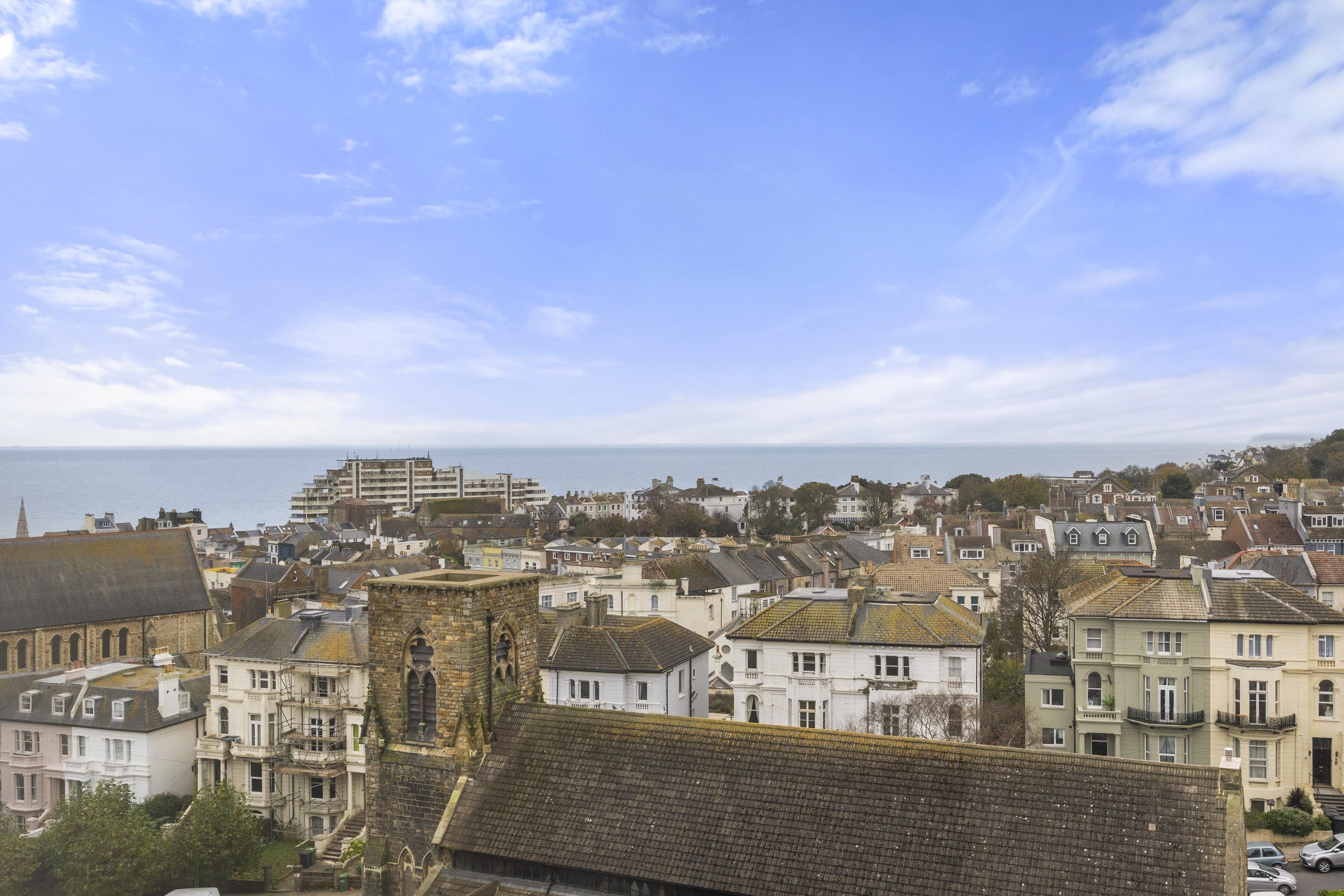 A coastal town with historic buildings, a prominent church tower, and a view of the sea.