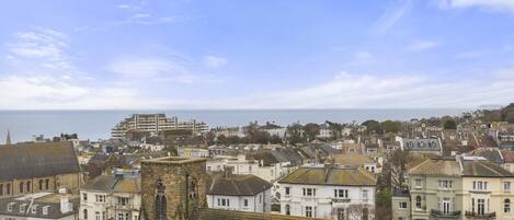 A coastal town with historic buildings, a prominent church tower, and a view of the sea.