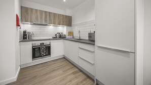 Une cuisine moderne avec des meubles blancs, un meuble supérieur en bois, un four encastré et un réfrigérateur en acier inoxydable.