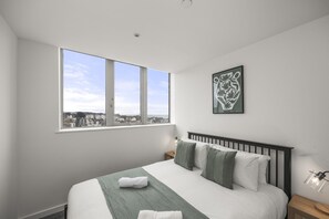 A hotel room with a large window, a bed with green bedding, a nightstand, and a wall-mounted lamp. - Ocean View A Free Parking By My Getaways (St Leonards-On-Sea)
