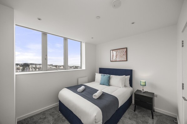 A modern hotel room with a large window, a neatly made bed, a bedside table with a lamp, and a city view. - Ocean View A Free Parking By My Getaways (St Leonards-On-Sea)