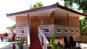 A building with a red staircase leading to a wooden door, surrounded by potted plants and outdoor chairs. - Plvillas (Pesalai)