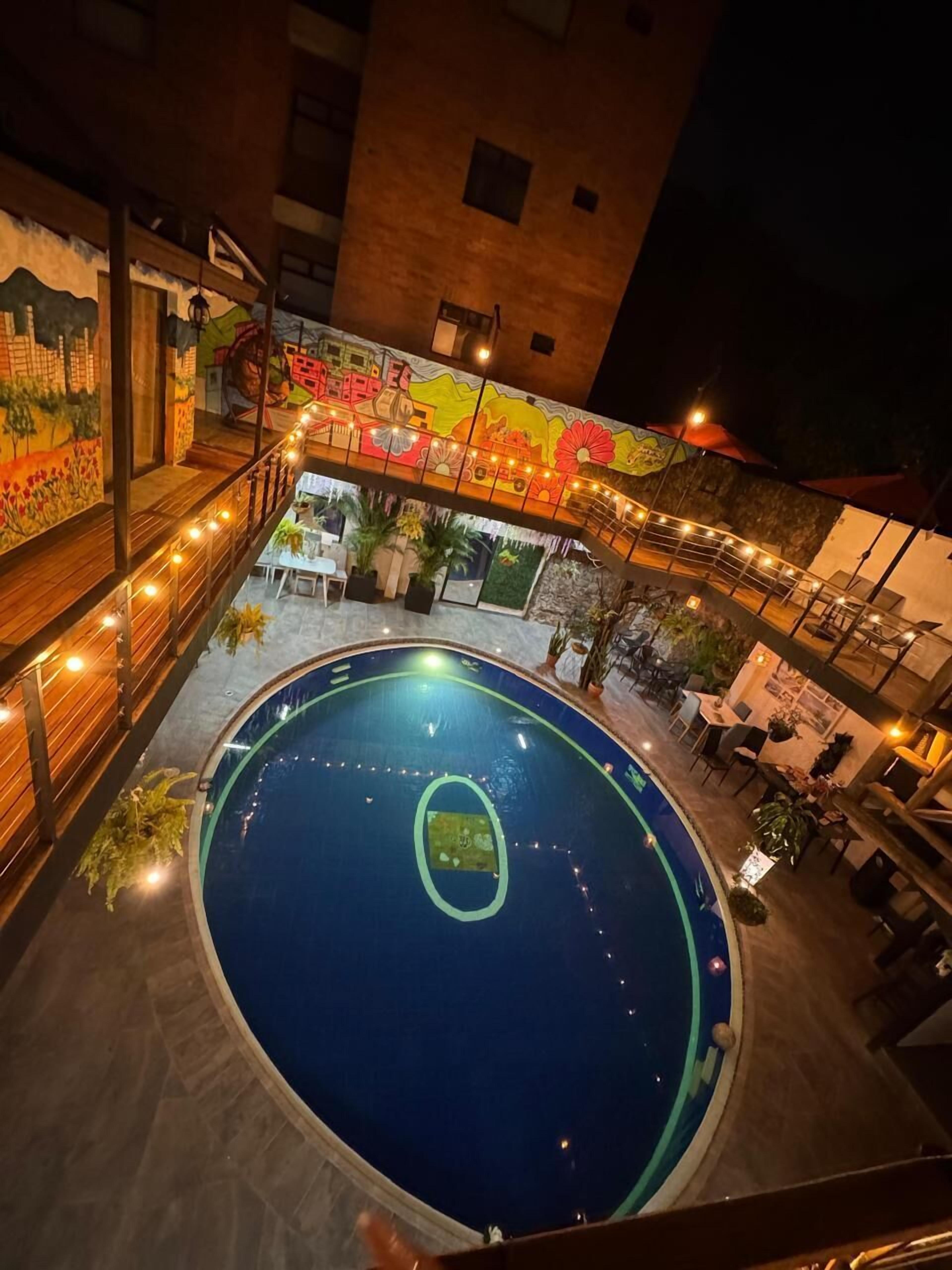 Una piscina interior con un mural en la pared, rodeada de zonas de estar y mesas.