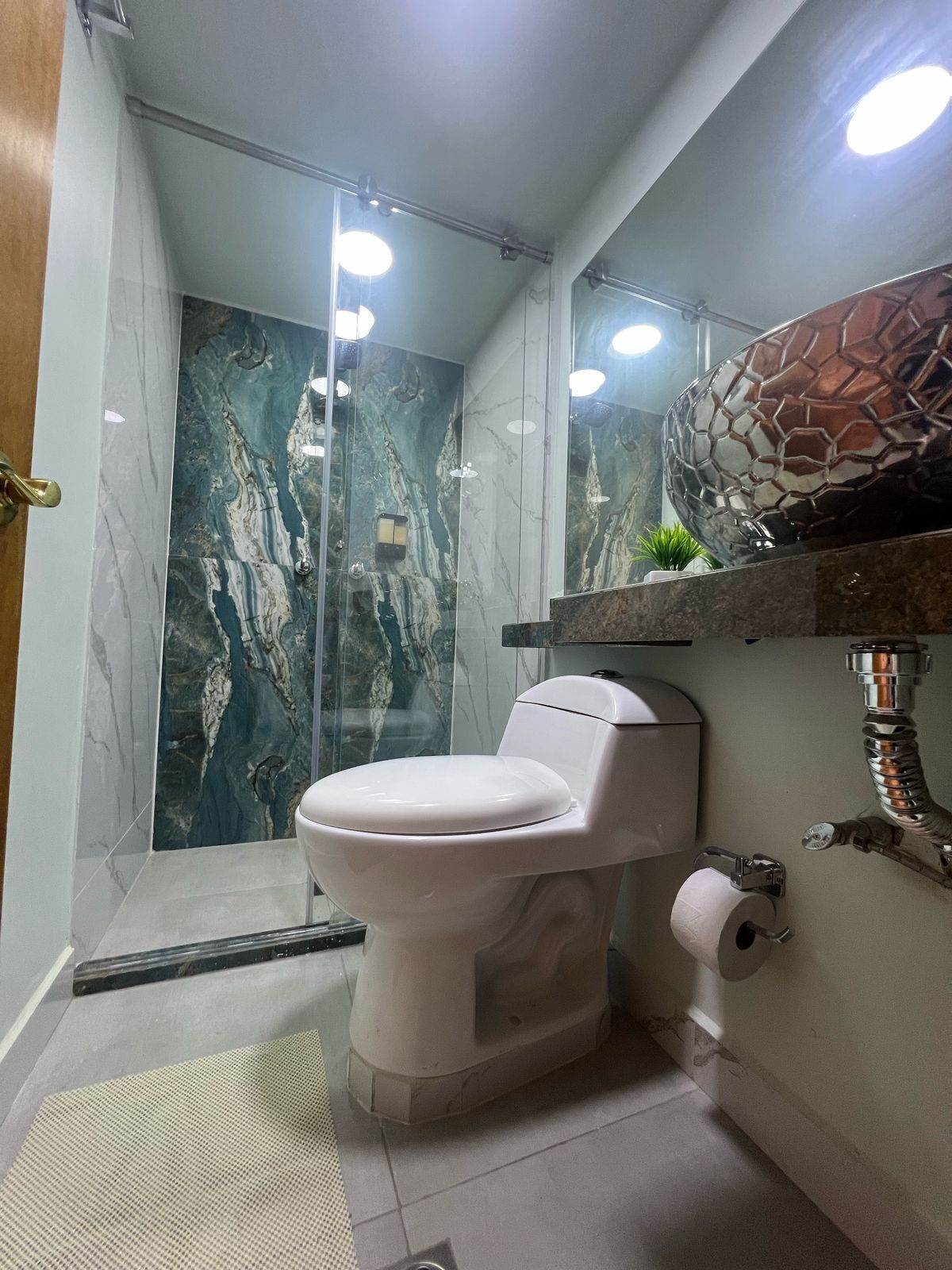 A modern bathroom with a marble shower wall, a toilet, and a sink with a decorative mirror.