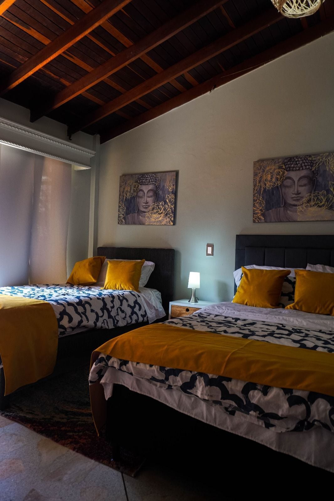A hotel room with two beds, a nightstand with a lamp, and artwork on the walls.