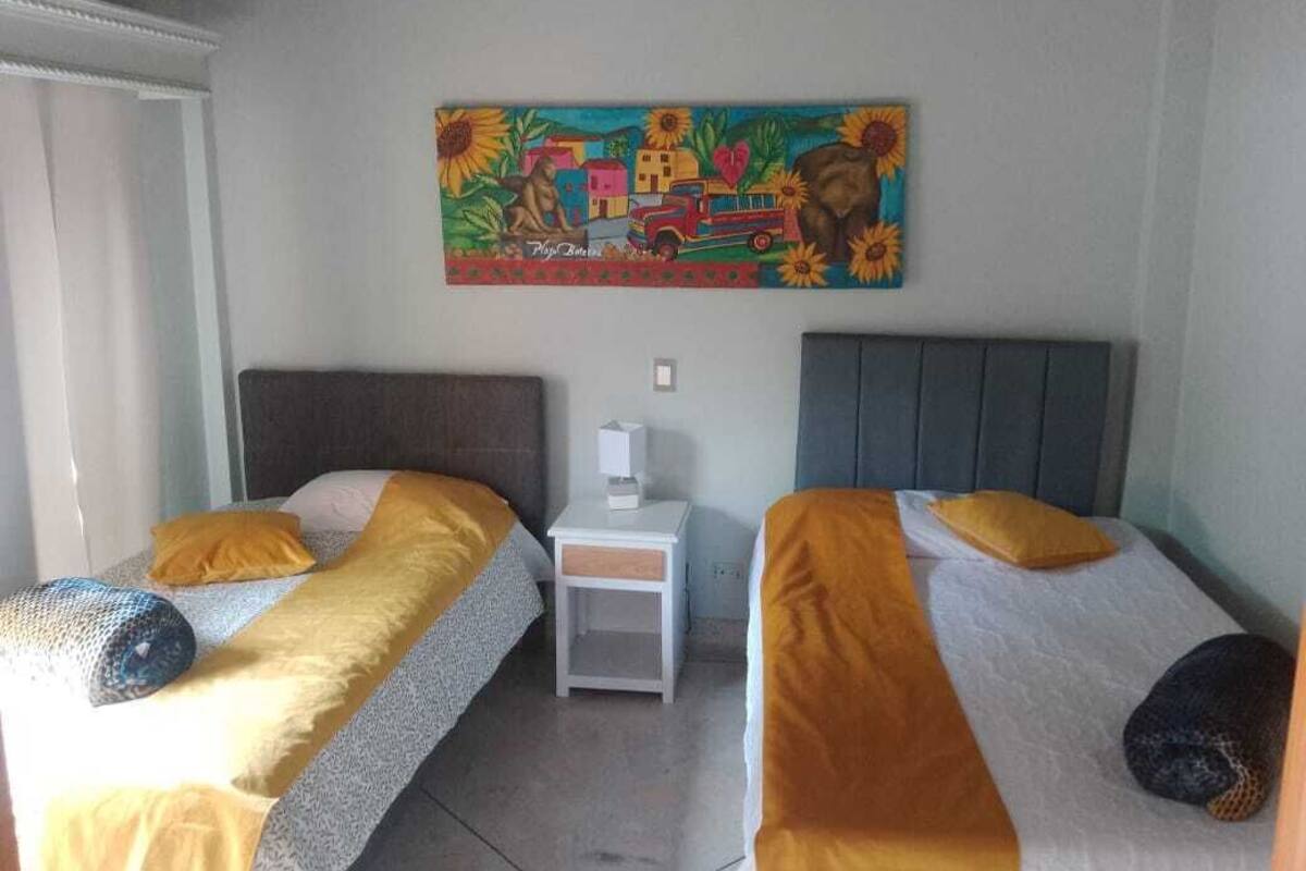 A room with two beds, each with a headboard, a small bedside table, and a wall-mounted painting.