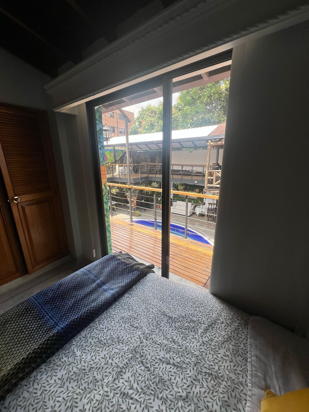 Une chambre avec un lit, une porte en bois et une vue sur l’espace extérieur abritant une piscine.