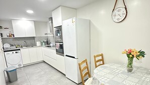 A modern kitchen with white cabinets, a built-in oven, and a refrigerator. There is a dining table with chairs and a vase of flowers. - Rooms Paris (Barcelona)