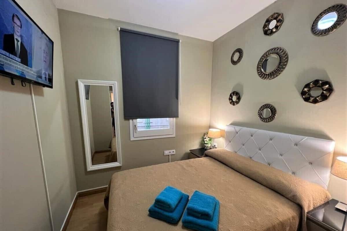 A hotel room with a bed, a television, a window with a blind, and decorative wall mirrors.