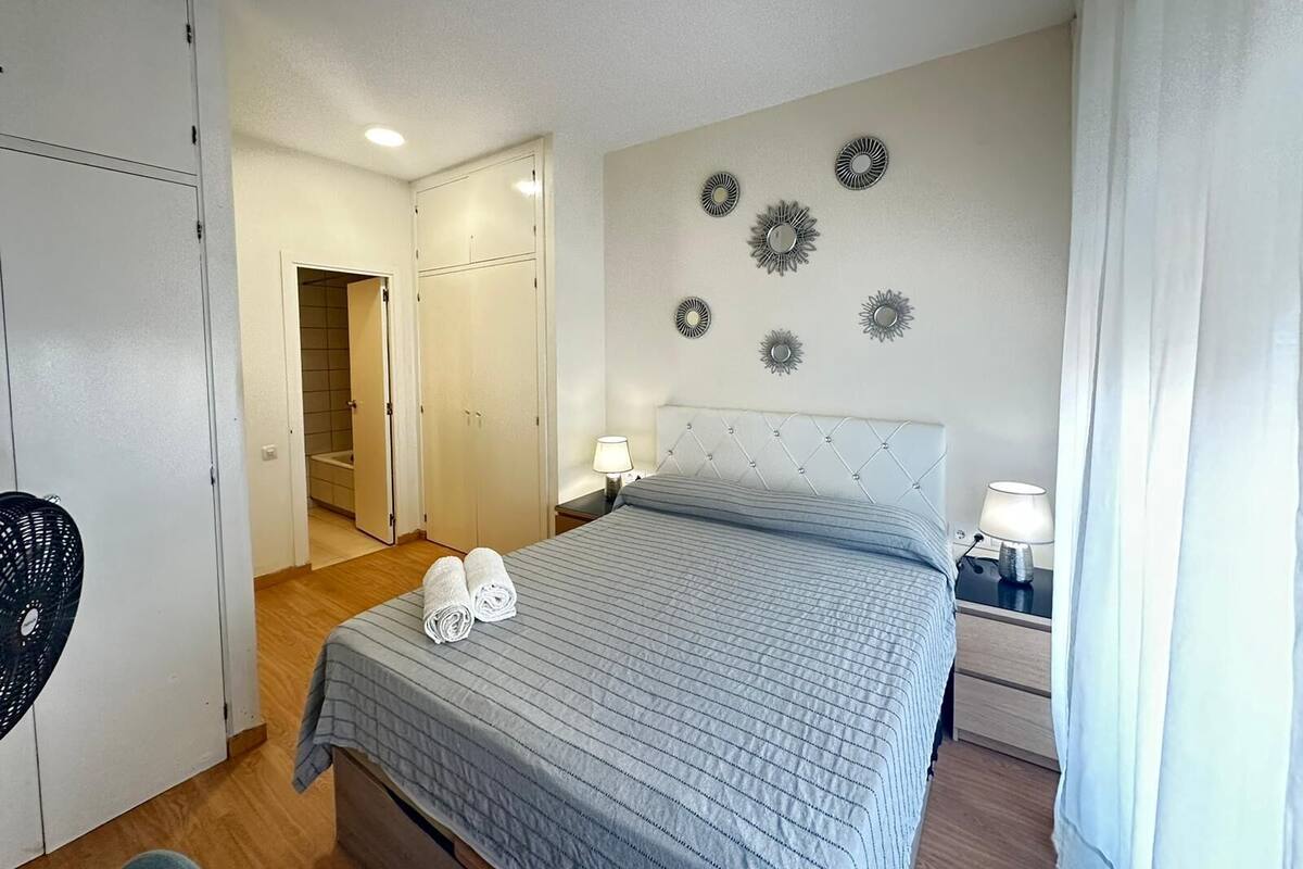 A bedroom with a bed, two bedside lamps, a wardrobe, and a door leading to a bathroom.