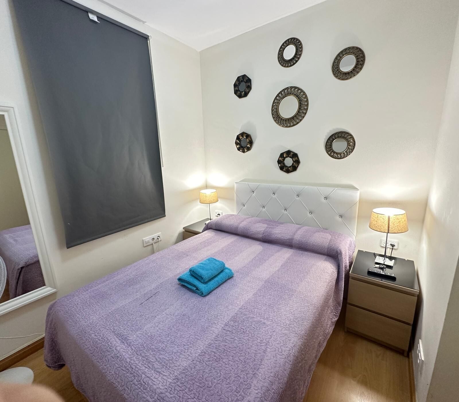 Un dormitorio ordenado con una cama grande, dos mesitas de noche con lámparas, un espejo en la pared y decoración mural.