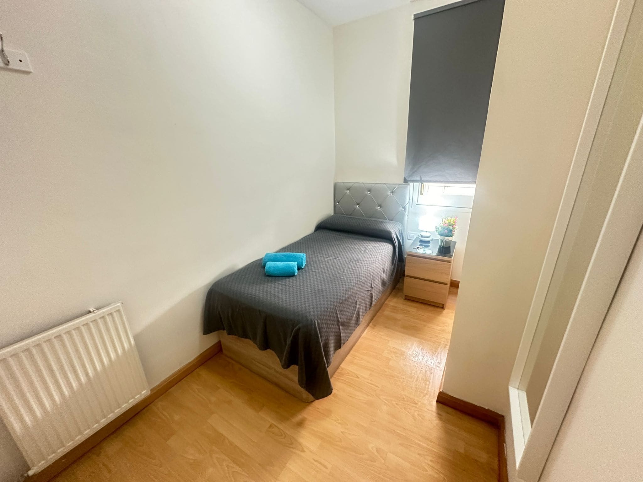 A small, neatly arranged bedroom with a single bed, a bedside table with a lamp, and a radiator.