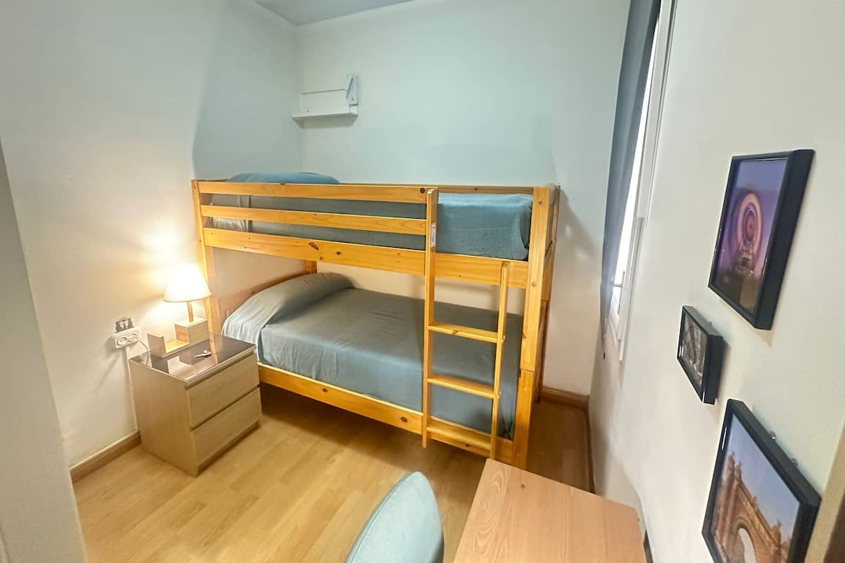 A bunk bed with a desk and a nightstand, a lamp, and framed pictures on the wall.