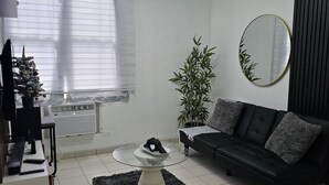Uma sala de estar moderna com um sofá preto, uma mesa de centro redonda, uma planta em vaso e um pinheiro de Natal.