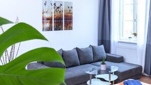 A modern living room with a grey sofa, a glass coffee table, and a large window with curtains. - Beautiful living near Schönbrunn (Wien)