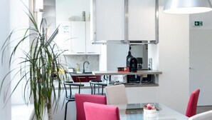 A modern kitchen with white cabinets, a stainless steel range hood, and a coffee machine. There is a dining area with a glass table and red chairs. - Beautiful living near Schönbrunn (Wien)