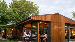 An outdoor seating area with tables and chairs, surrounded by a wooden structure with glass walls, under a clear sky. - No Pardon Hotel (Satu Mare)