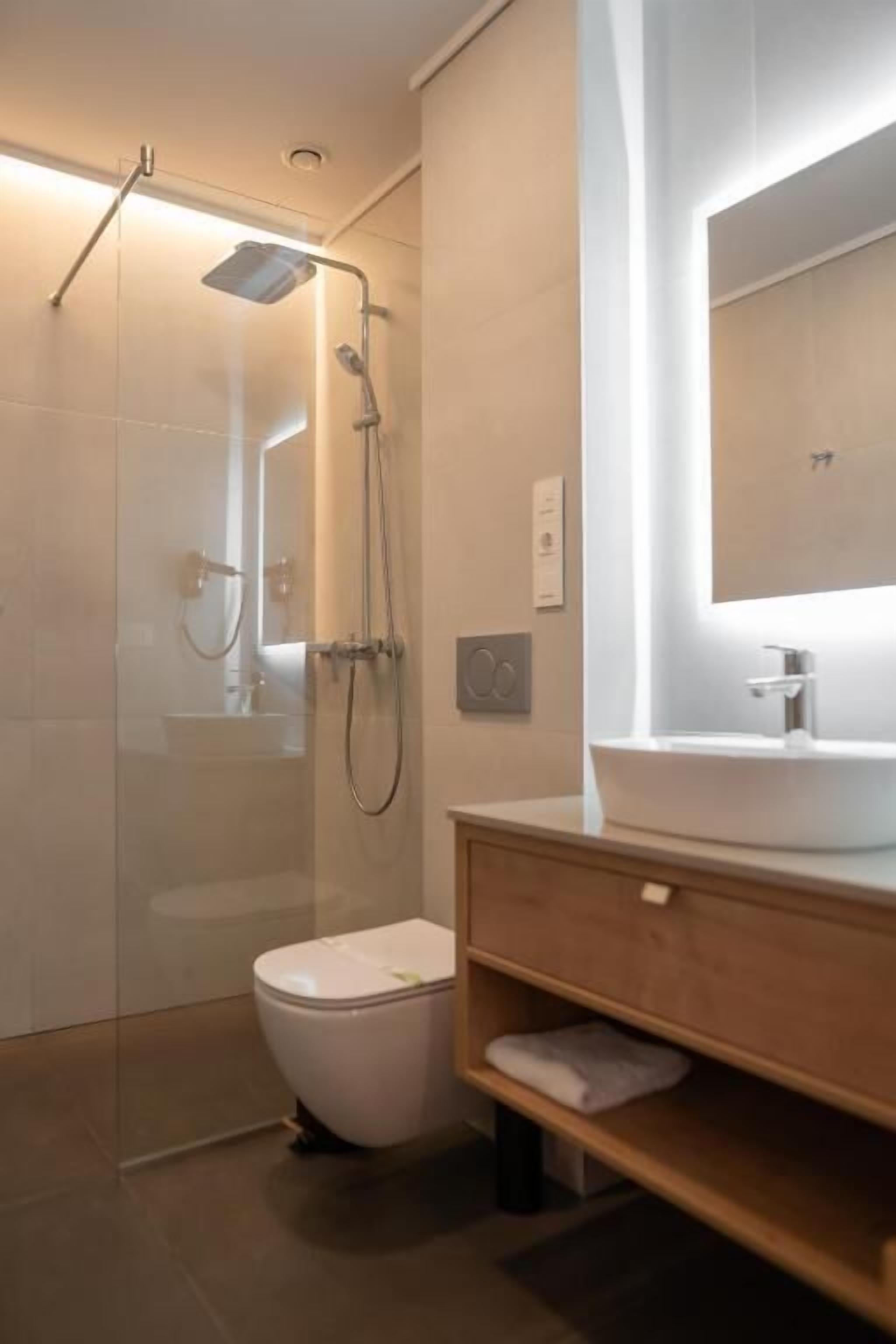 A modern bathroom with a glass-enclosed shower, a white toilet, and a wooden vanity with a mirror.