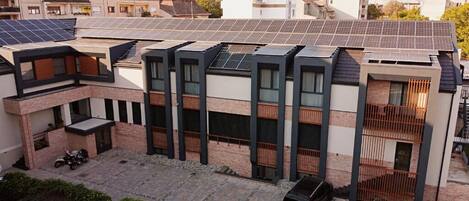 A modern residential building with solar panels on the roof, a covered parking area, and a black car parked in front.