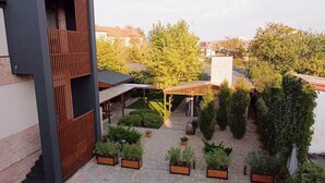 Une cour intérieure avec un bâtiment moderne, un espace de repos abrité et diverses plantes en pot.