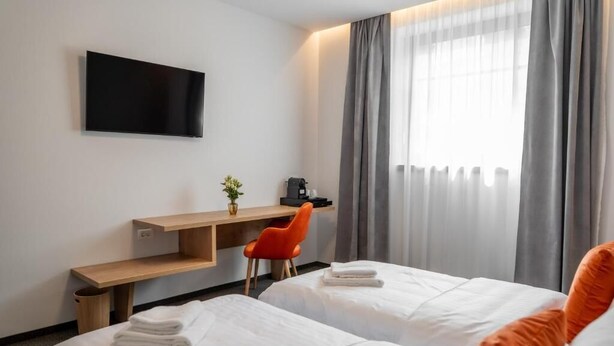 A hotel room with two beds, a desk, a chair, a TV, and a window with curtains. - No Pardon Hotel (Satu Mare)