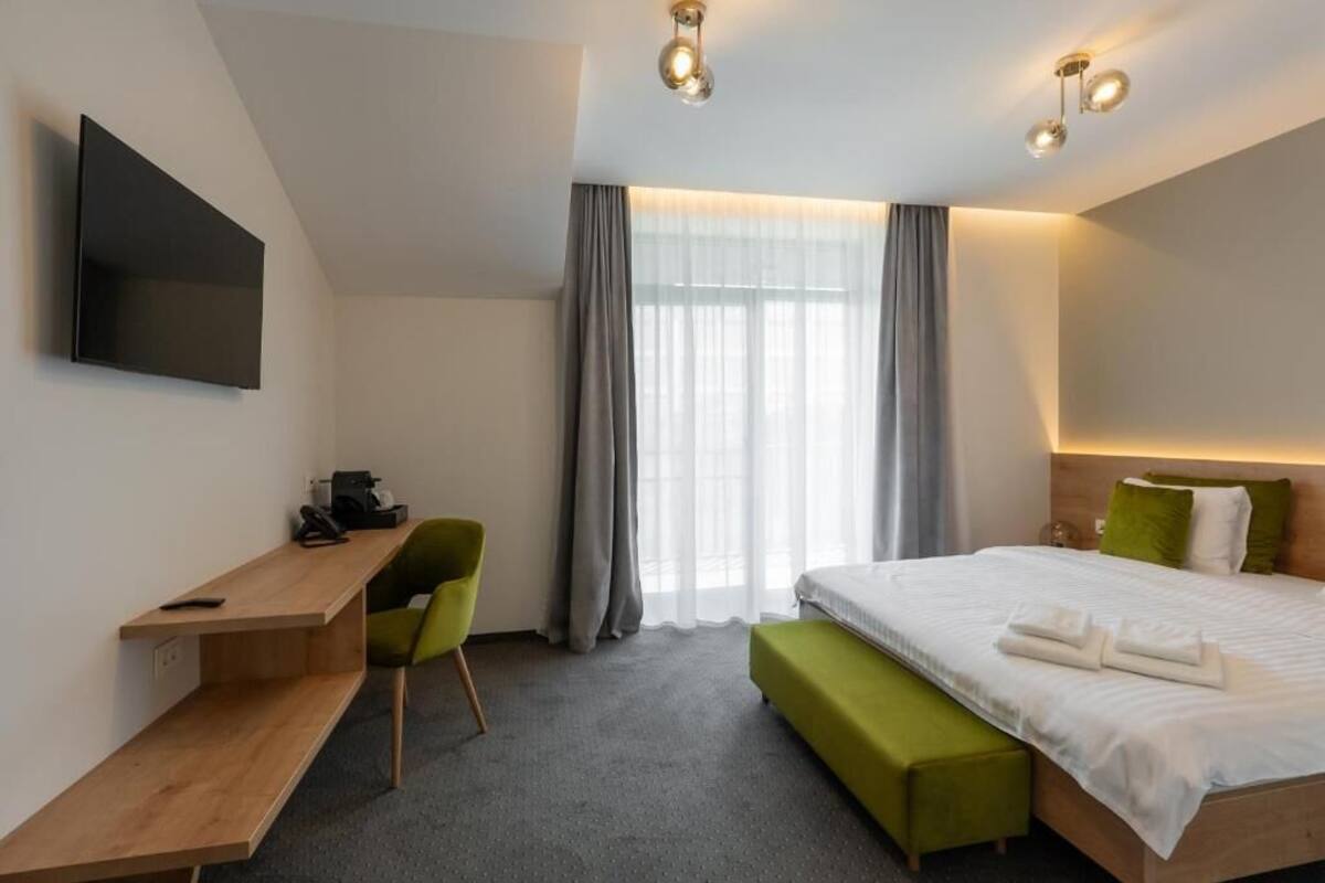 Ein Hotelzimmer mit einem Bett, einem Schreibtisch, einem Sessel, einer Bank und einem an der Wand montierten Fernseher.
