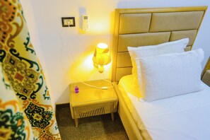 A hotel room with a bed, a bedside table with a lamp, a phone, and a wall socket.