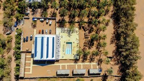 An aerial view of a resort with a pool area, multiple vehicles, and palm trees. - Ecolodge Ksar Ghilane (Douz Sud)