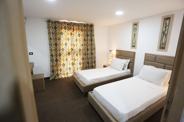 Una habitación de hotel con dos camas individuales, una mesita de noche pequeña, una lámpara de noche y una cortina estampada, además de una obra de arte colgada en la pared.