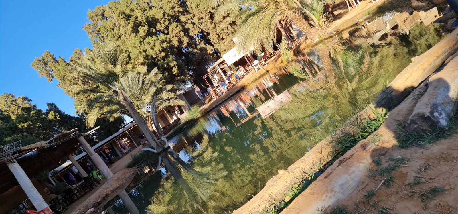 Una zona junto al río con una estructura de madera, posiblemente un restaurante o café, y un gran árbol.