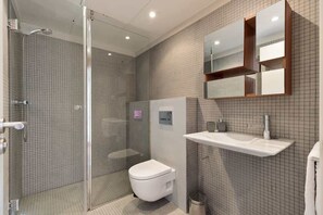 Een moderne badkamer met een glazen douchecabine, een wit toilet en een wandgemonteerde wastafel met een spiegel erboven.