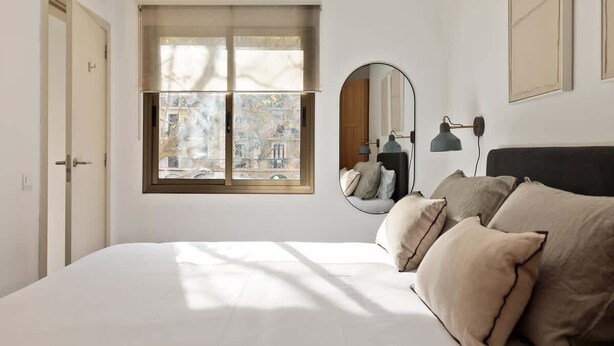 Ein Schlafzimmer mit einem großen Bett, einem Fenster mit Aussicht, einem runden Spiegel und einer Lampe.