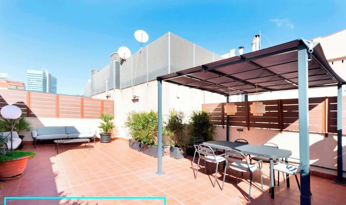 Una terrazza sul tetto con zona salotto coperta, piante in vaso e un tavolo con sedie.