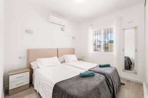 A double bed with white bedding and two pillows, a bedside table with a lamp, and a window with a view of the outside.