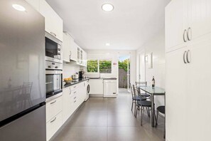 A modern kitchen with white cabinetry, stainless steel appliances, and a dining area with a glass table and chairs. - Villa Esmerelda Sun - Four Bedroom Villa, Sleeps 8 (Bel-Air)