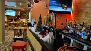 Un espace bar avec un téléviseur diffusant des clips musicaux, un sapin de Noël et diverses bouteilles.