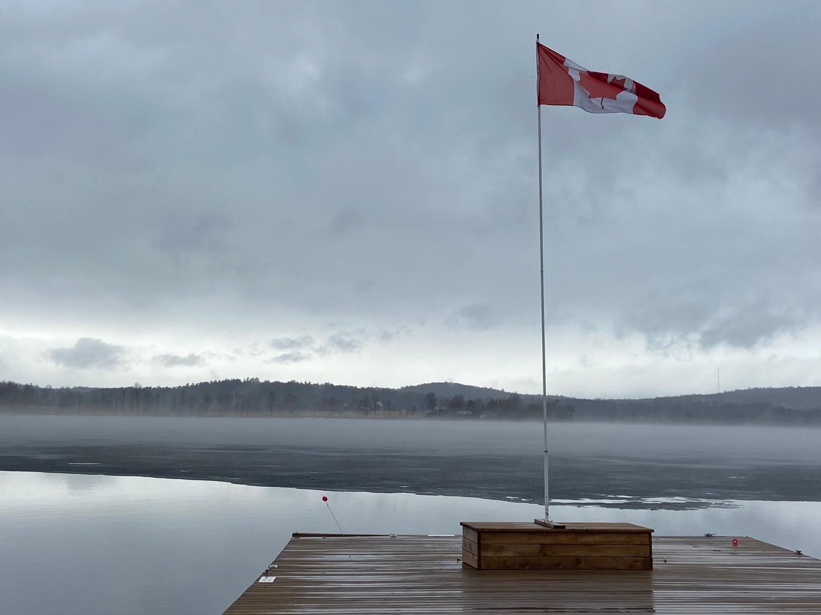 Eine Holzstege, der sich in ruhiges Wasser erstreckt, mit einer kanadischen Flagge auf einem Mast.