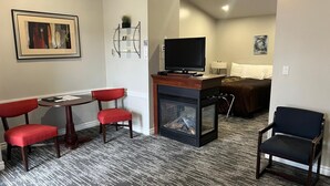 Une chambre d’hôtel avec une cheminée, une télévision, un coin repas avec des chaises rouges et un lit en arrière-plan.