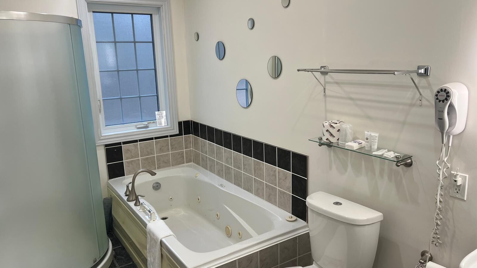 Une salle de bain moderne avec une baignoire sur pieds, des toilettes, une étagère en verre où sont rangés les articles de toilette et un sèche-cheveux fixé au mur.