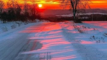 Un paisaje nevado con un atardecer, cielo despejado y un sendero que se adentra en la distancia.