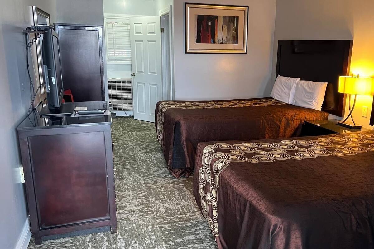 A hotel room with two beds, a TV, a desk, and a framed picture on the wall.