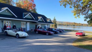 Un bâtiment doté d’un toit végétalisé et de bordures blanches, un parking où sont garées plusieurs voitures anciennes, et un lac en arrière-plan.