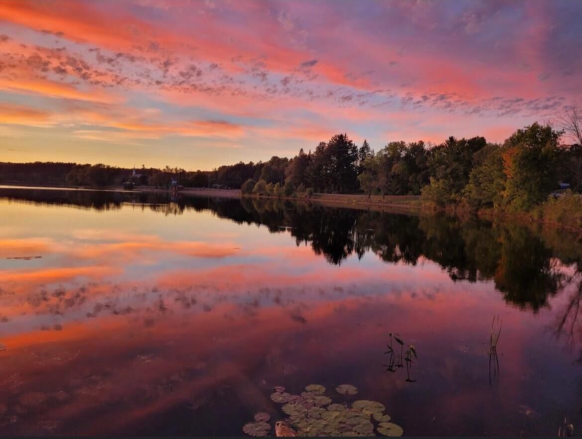 Un lago tranquilo al atardecer con reflejos de árboles y cielo.