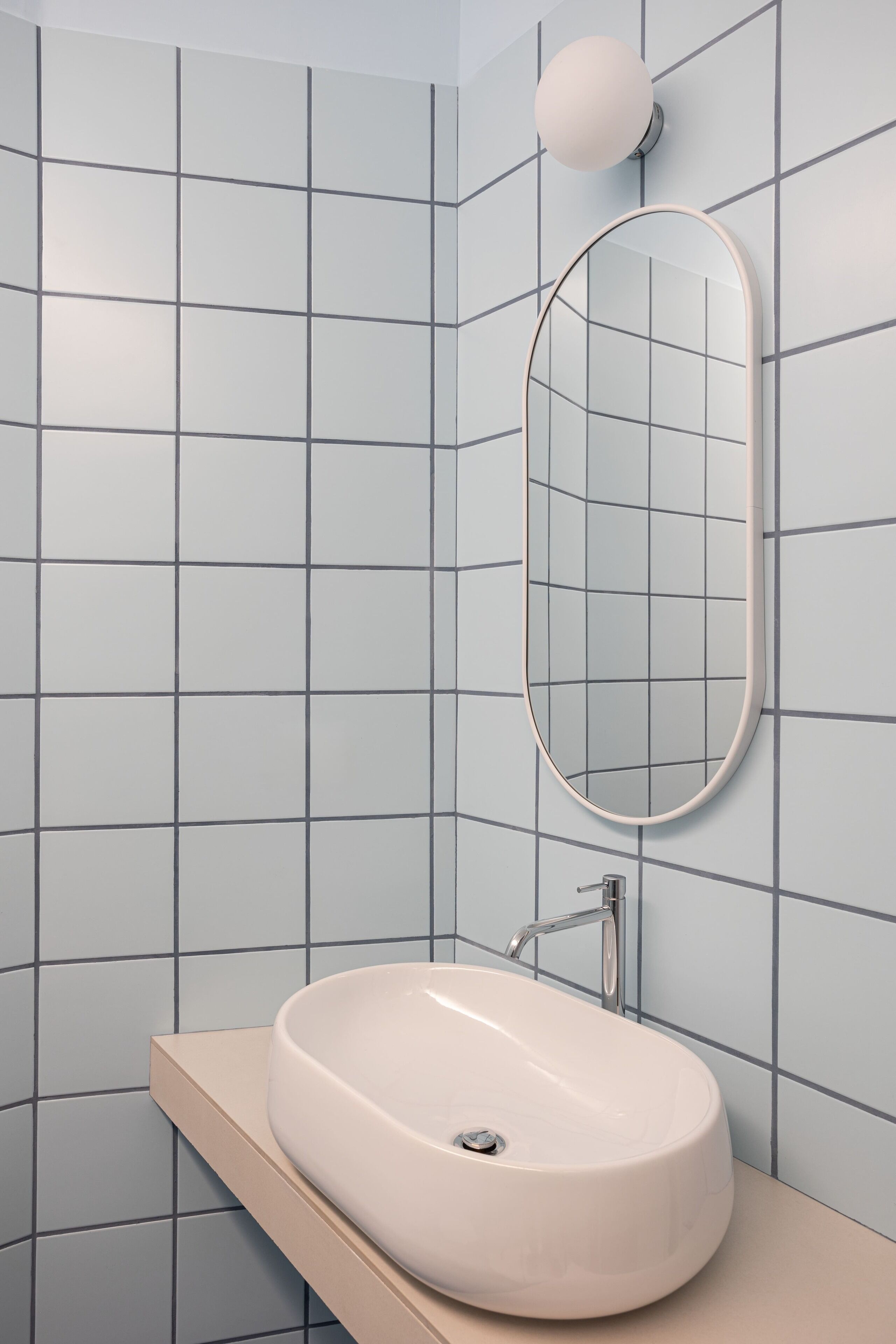 A bathroom with a white sink, a mirror, and a light fixture on the wall.