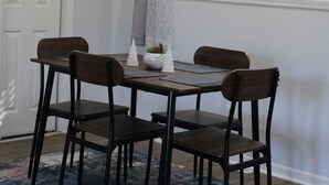 Un área de comedor con una mesa y cuatro sillas, una planta decorativa y una alfombra estampada.