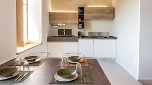 A modern kitchen with a dining area, featuring a marble countertop, a built-in oven, and a wooden ceiling.