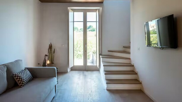 A modern living room with a sofa, a TV mounted on the wall, and a staircase leading to an outdoor area.