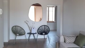 A modern living room with a wooden ceiling, a sofa with checkered pillows, two black chairs, and a round mirror on the wall.