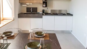 A modern kitchen with a dining area. It features a wooden ceiling, a built-in stove, and a small shelf with kitchen items.